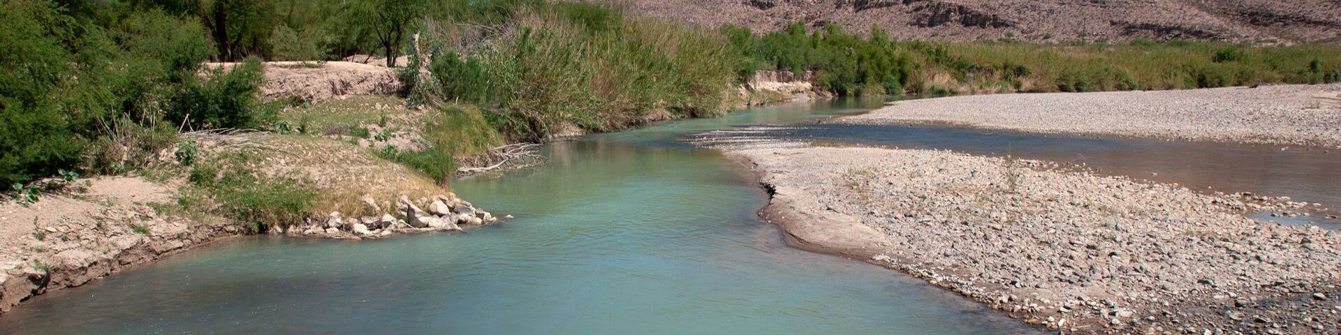 A river flowing through a rocky landscape with green vegetation and mountains in the background.