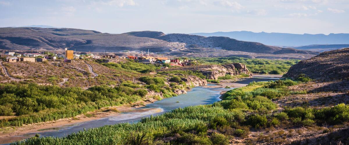 A river winding through a green valley with hills in the background and a clear sky.
