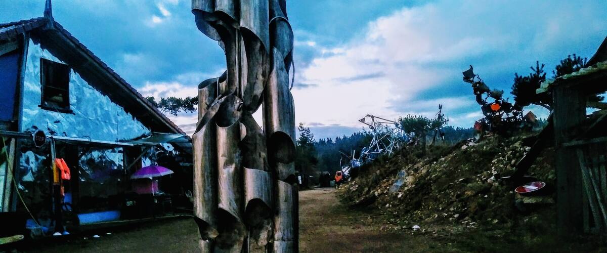 A rustic sculpture in a rural setting with a dirt road, houses, and a cloudy sky.