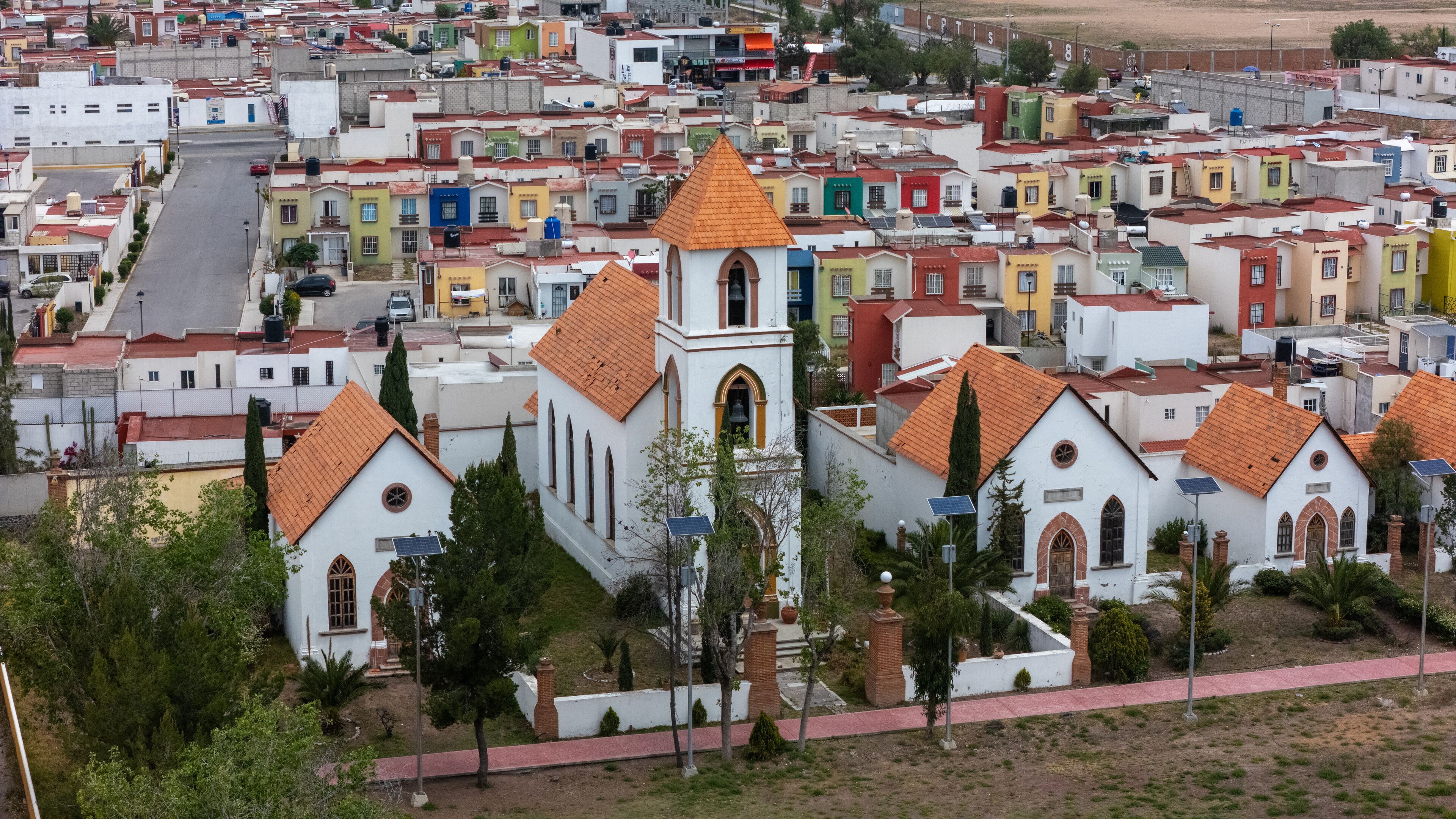A white church with a red roof and bell tower surrounded by colorful houses.