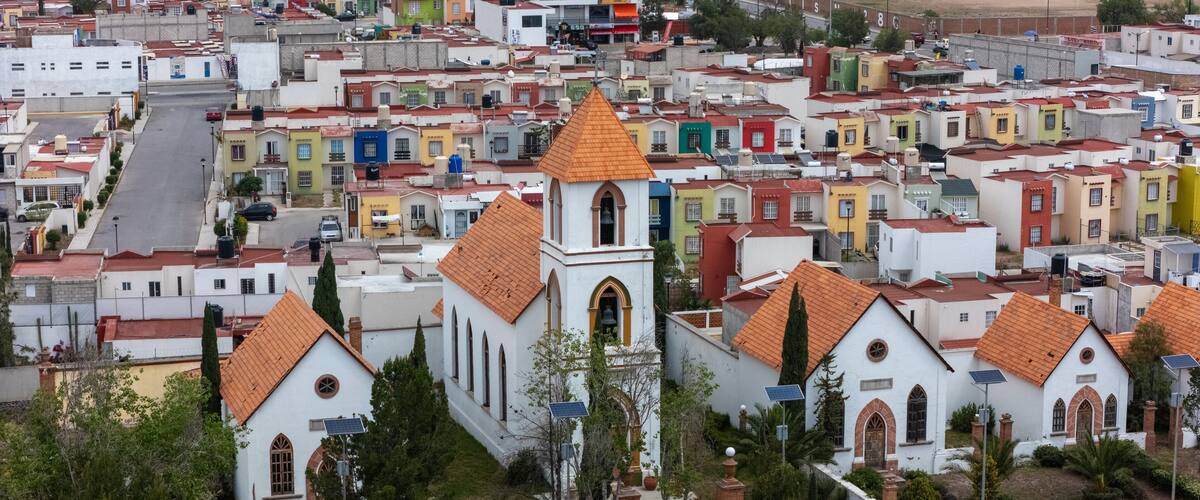 A white church with a red roof and bell tower surrounded by colorful houses.