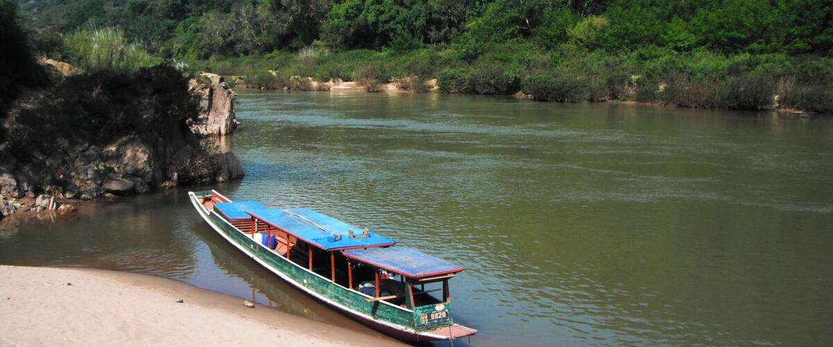 A river with a boat docked on the sandy bank.