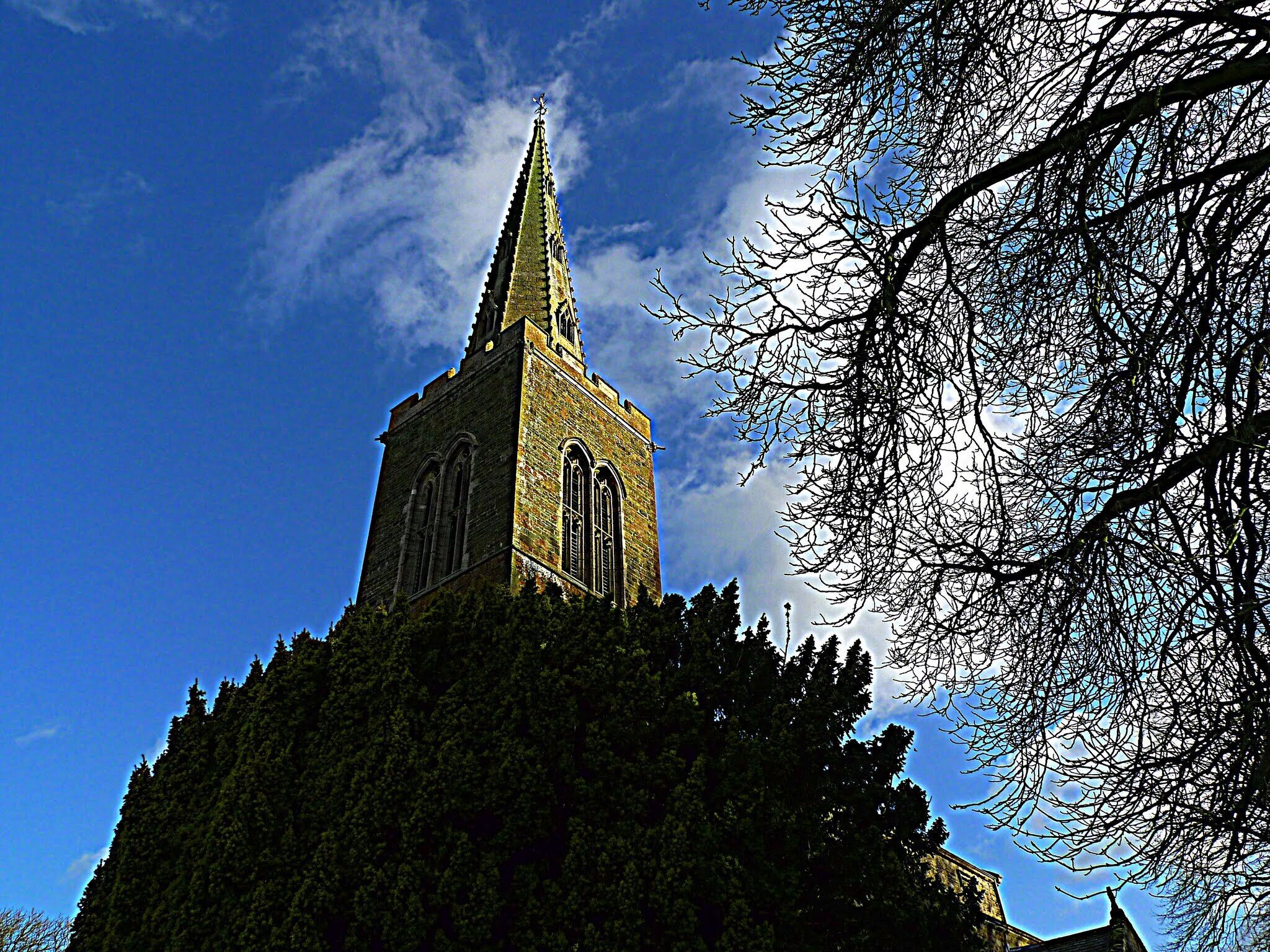 A church with a tall spire and arched windows, surrounded by trees and a clear blue sky.