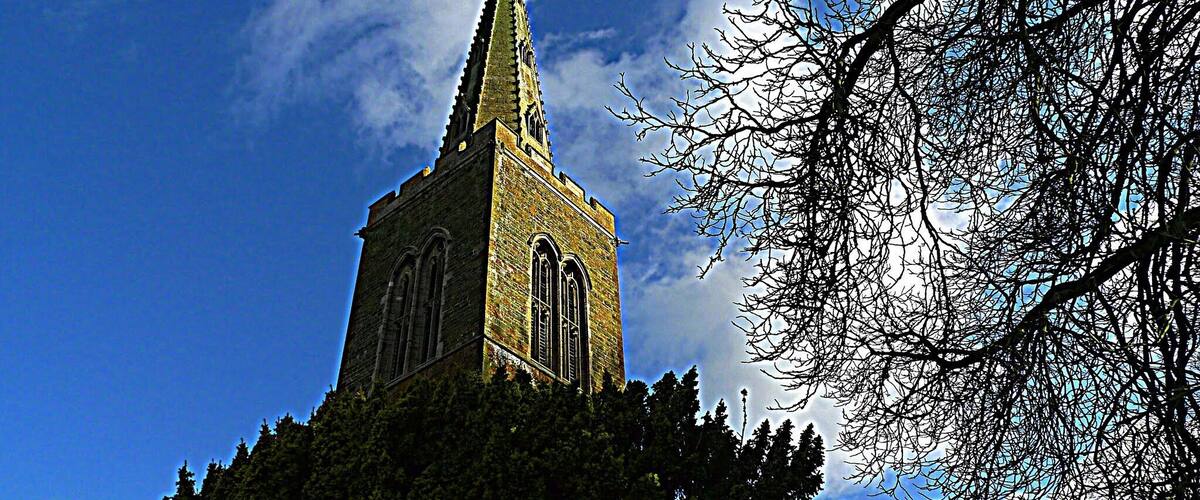 A church with a tall spire and arched windows, surrounded by trees and a clear blue sky.