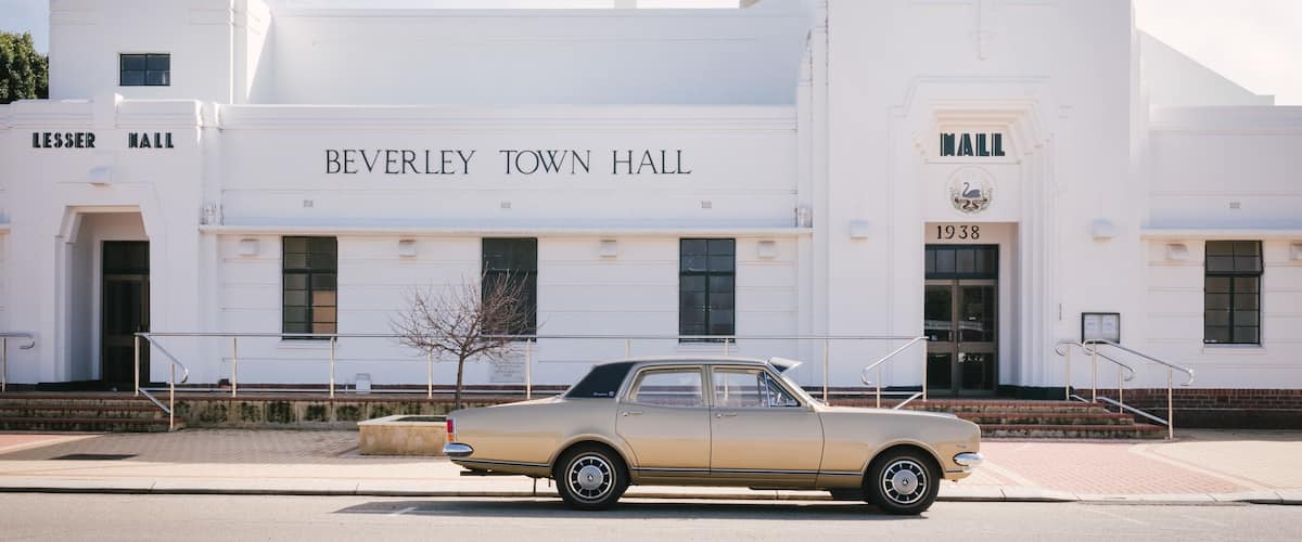 A vintage beige car parked in front of the Beverley Town Hall, which features a prominent '1938' date on its facade.