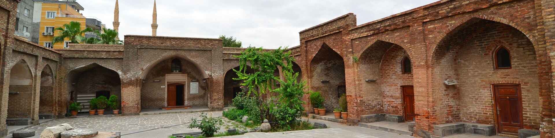 A courtyard with brick arches, a central garden, and a building with a minaret in the background.