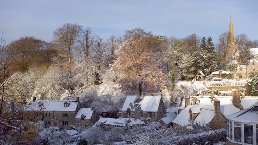 Ein schneebedecktes Dorf mit traditionellen Steinhäusern, einem Kirchturm und einer großen Nadelbaum.'
