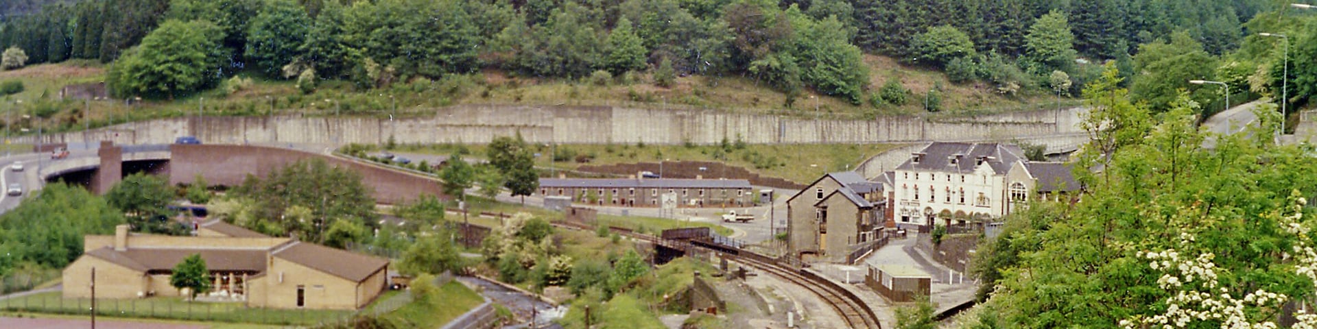 Junction at Aberbeeg of railways and valleys, 1990. View NW from the A463 road up the Ebbw Valley, towards Ebbw Vale (to the left, Ebbw Fawr), with the railway still open - just about) and to the right up the Ebbw Fach valley to Abertillery, Nantyglo and Brynmawr. In this 1990 view it appears that there are still station platforms for both routes, but the station had been closed for passengers on 30/4/62 and for goods from 28/11/66. The line up the Ebbw Fawr remained open to serve Ebbw Vale Steelworks and a passenger service to Ebbw Vale - but not stopping here - was restored on 6/2/08. The line to the right to Nantyglo and Brynmawr was closed from 30/4/62, although goods to Abertillery continued until 7/4/69, but it still seems to exist here in 1990.
