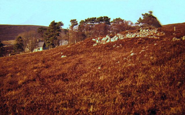A hilly landscape with a stone wall, trees, and a small house.