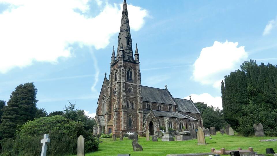 A historic church with a tall spire, surrounded by a cemetery with headstones and crosses.