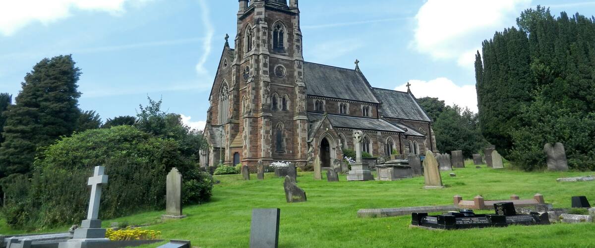 A historic church with a tall spire, surrounded by a cemetery with headstones and crosses.