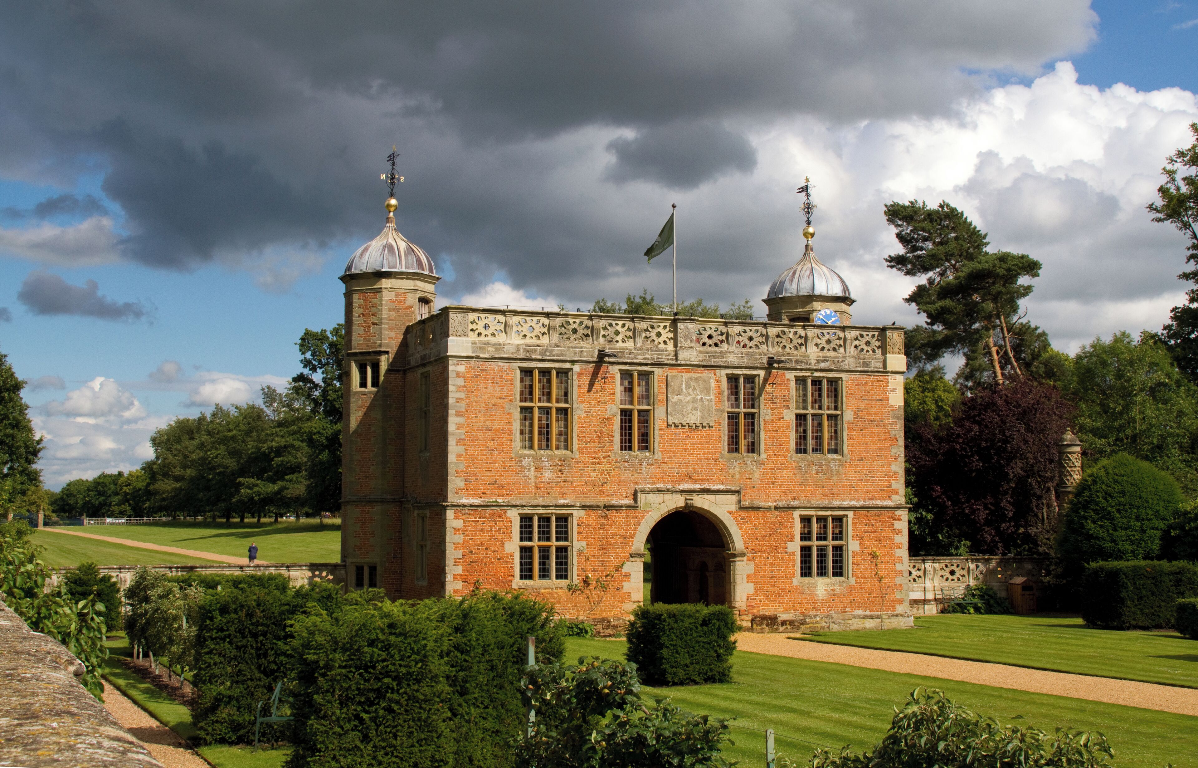 A historic building with two domed towers, surrounded by well-maintained gardens and a clear sky.