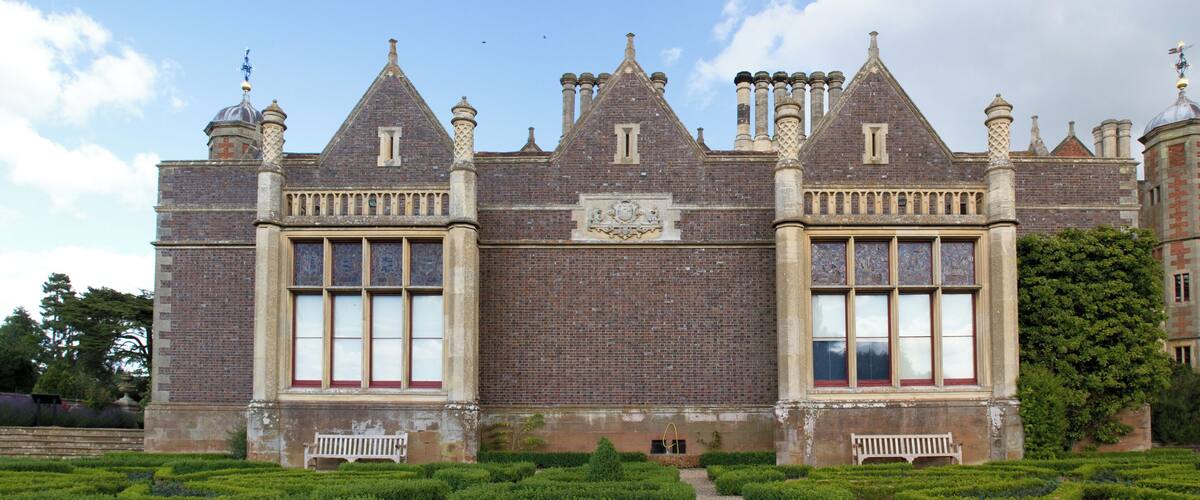 A large, historic building with a symmetrical facade, large windows, and a central emblem.