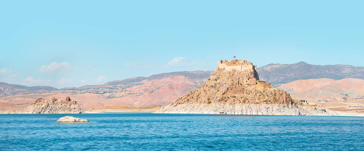 A coastal landscape with a prominent rocky hill and a small island in the foreground.