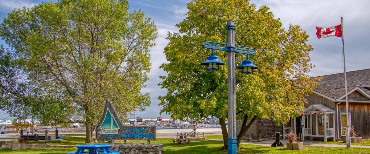 A park with a picnic table, a signboard, a flagpole with a flag, and a building with a wooden exterior.
