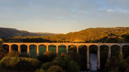 A stone viaduct over a river with a forested hillside in the background.