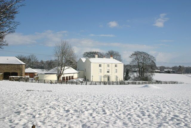 A snow-covered landscape with a white house, a barn, and a fence.