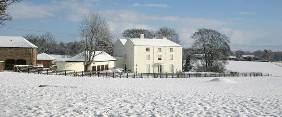 A snow-covered landscape with a white house, a barn, and a fence.