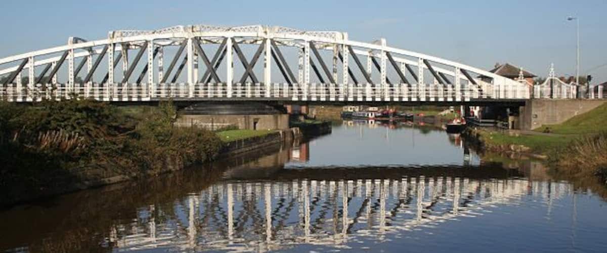 A white steel bridge over a calm river with a clear reflection.