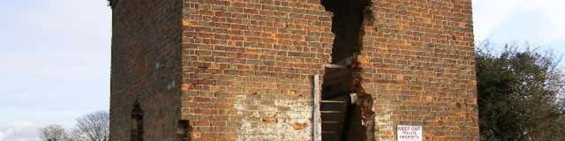 Edificio de ladrillo con un gran agujero en la pared, rodeado por una valla y un área con césped.