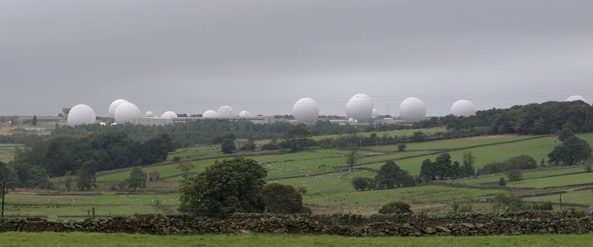 A rural landscape with rolling hills, a stone wall, and a line of white spherical structures.