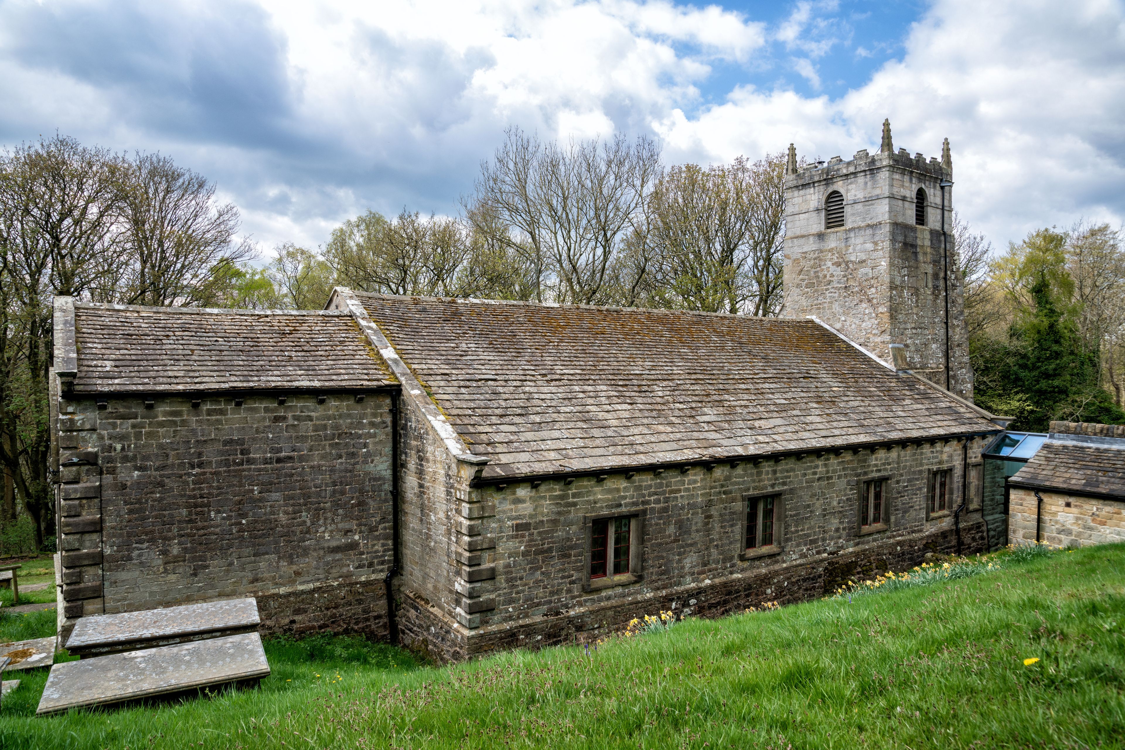 A historic stone building with a tower, surrounded by trees and grass.