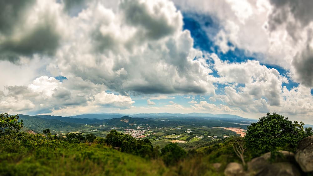 A mountainous landscape with a town in the valley, dense forests, and a cloudy sky.