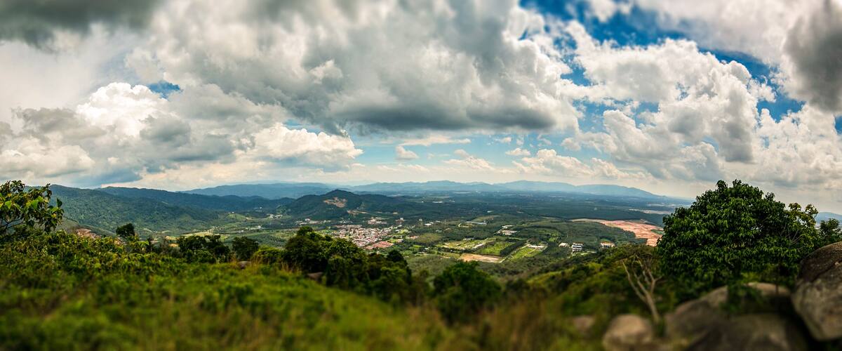 A mountainous landscape with a town in the valley, dense forests, and a cloudy sky.