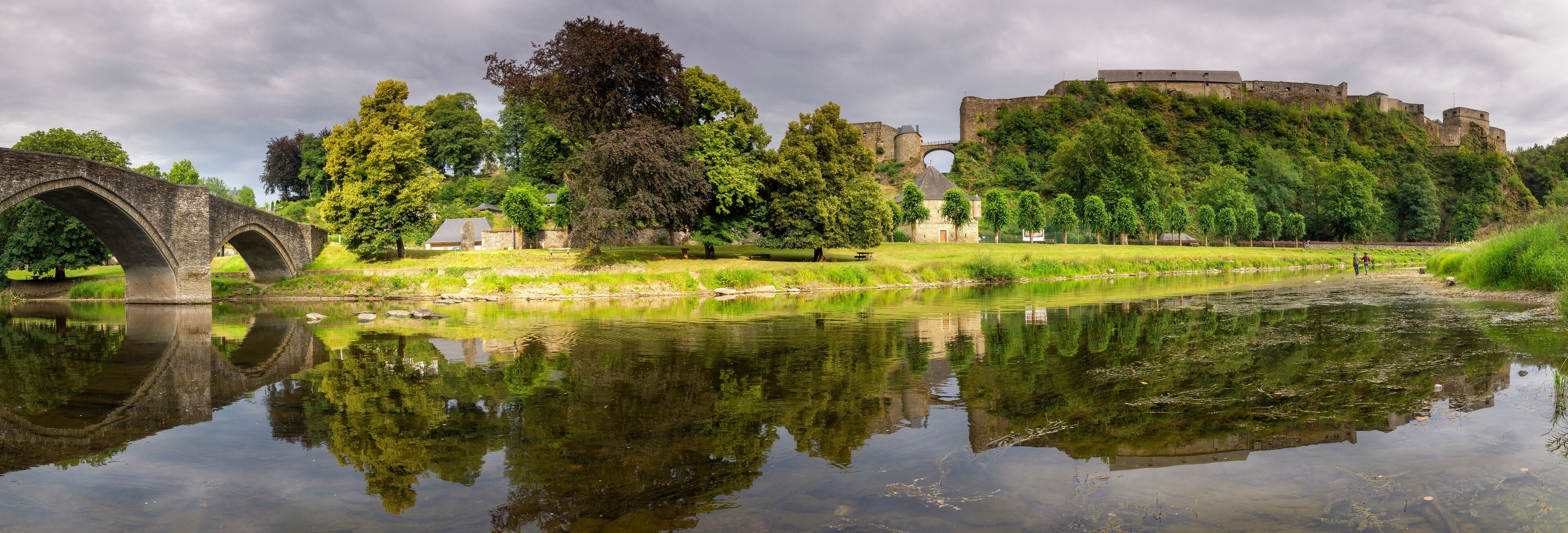 A historic bridge, a castle, and a calm river reflecting the surrounding greenery.