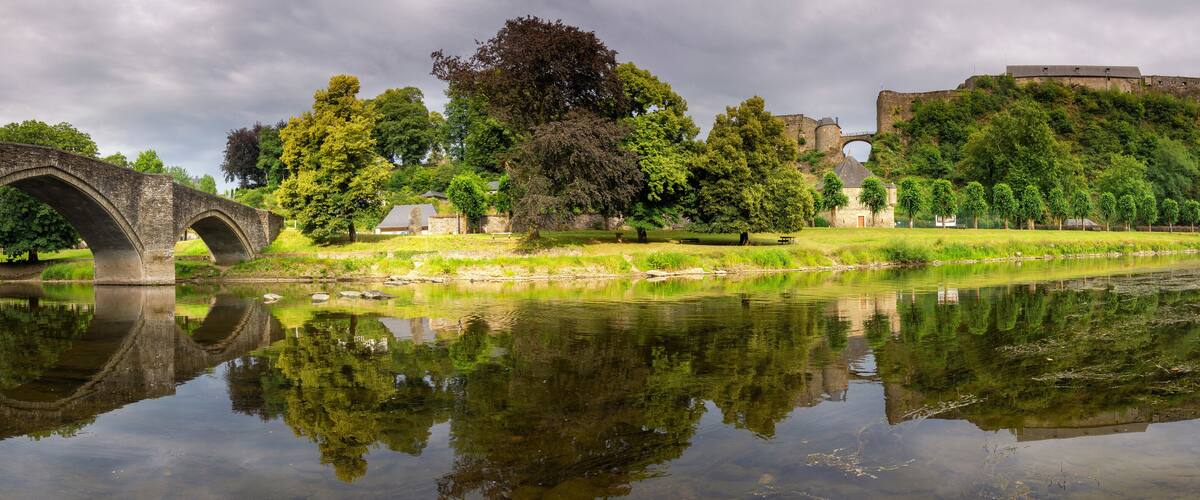 A historic bridge, a castle, and a calm river reflecting the surrounding greenery.