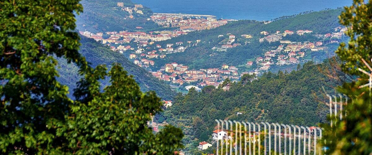 A coastal town nestled in a valley with a view of the sea and a hilltop fortress.