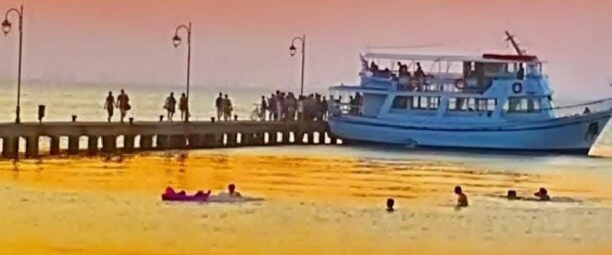 A sunset at a beach with a pier and a blue boat.