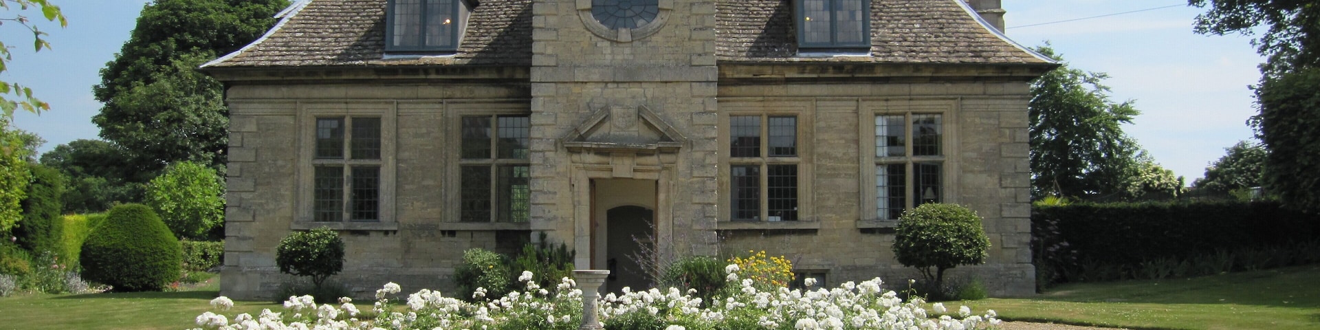 A large stone house with a symmetrical facade, a central entrance, and a circular window above the door.