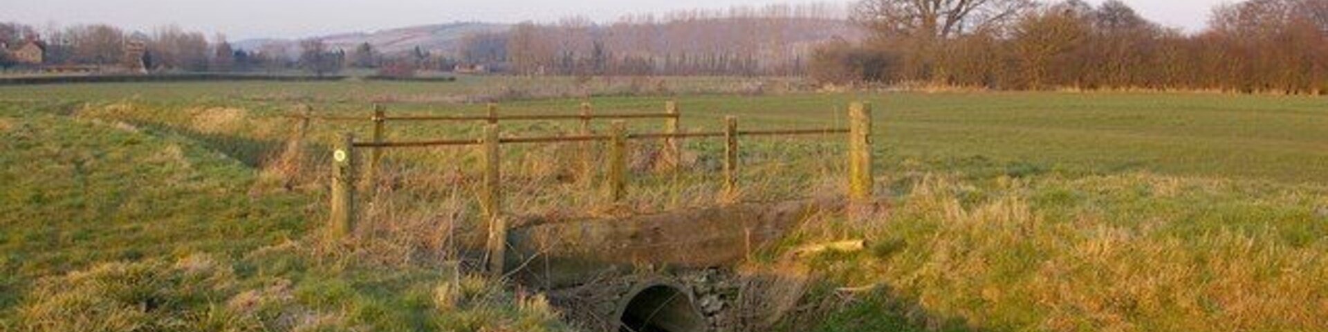 Bridge over drainage ditch, Wigmore Moor This is one of a number of drainage ditches on Wigmore Moor, a small area of levels south of the River Teme. In the background near the left hand edge of the photo are the remains of Wigmore Abbey.