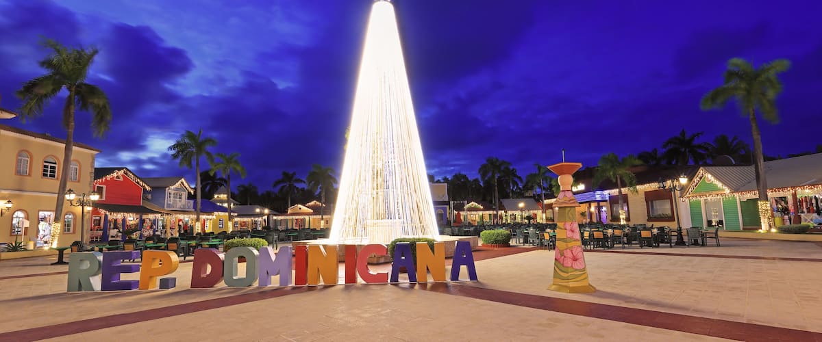 A night scene with a lit fountain, palm trees, and buildings with colorful lights.