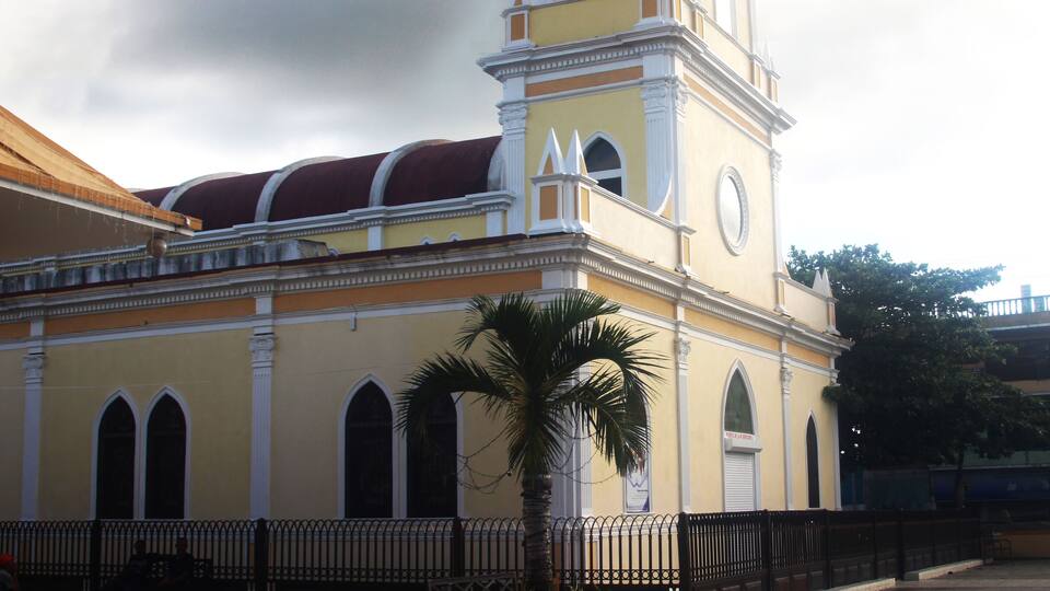 A yellow church with a clock tower and a red roof.