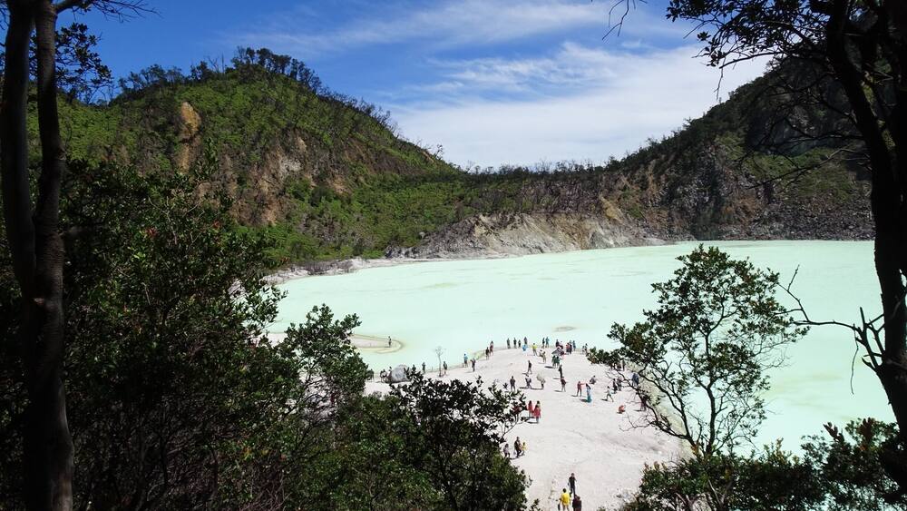 A turquoise lake surrounded by forested hills with a group of people on the shore.