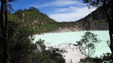 Un lago turquesa rodeado de colinas boscosas con un grupo de personas en la orilla.