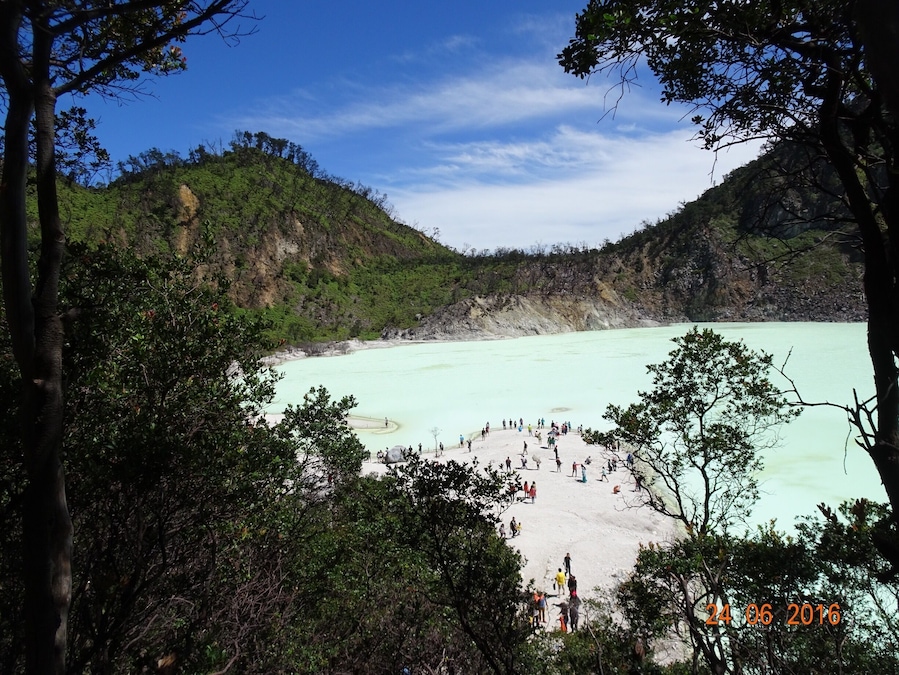Um lago azul-turquesa cercado por colinas arborizadas, com um grupo de pessoas na margem.