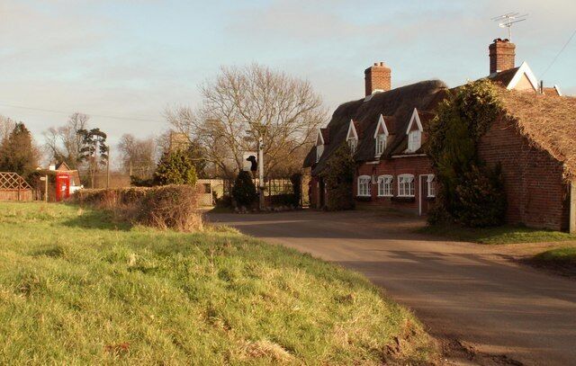 A rural road with traditional houses, a red telephone box, and a clear sky.