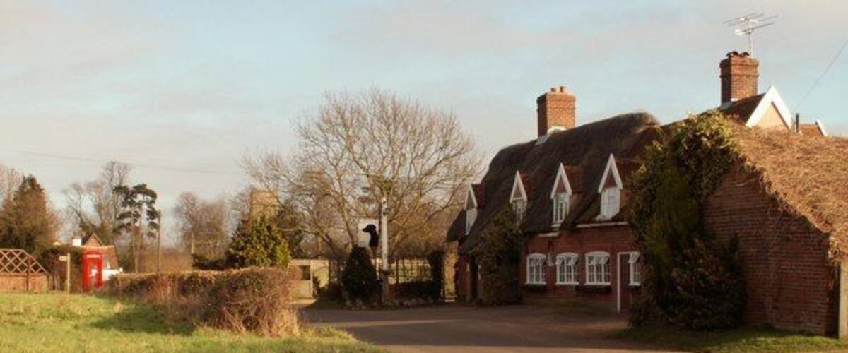 A rural road with traditional houses, a red telephone box, and a clear sky.