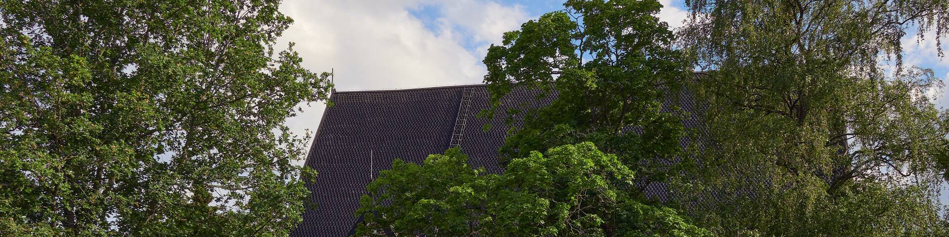 A historic stone building with a tiled roof, surrounded by lush green trees and a stone wall.