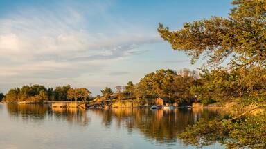 A calm lake with boats, trees, and a small wooden structure on the shore.