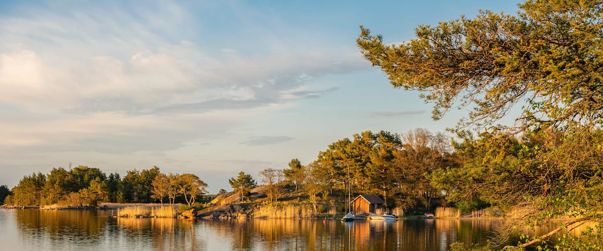A calm lake with boats, trees, and a small wooden structure on the shore.