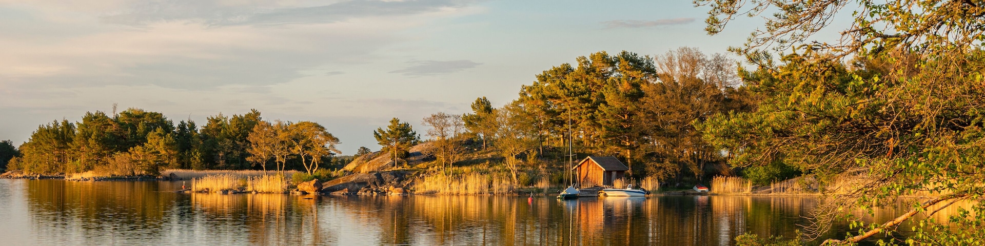 A calm lake with boats, trees, and a small wooden structure on the shore.