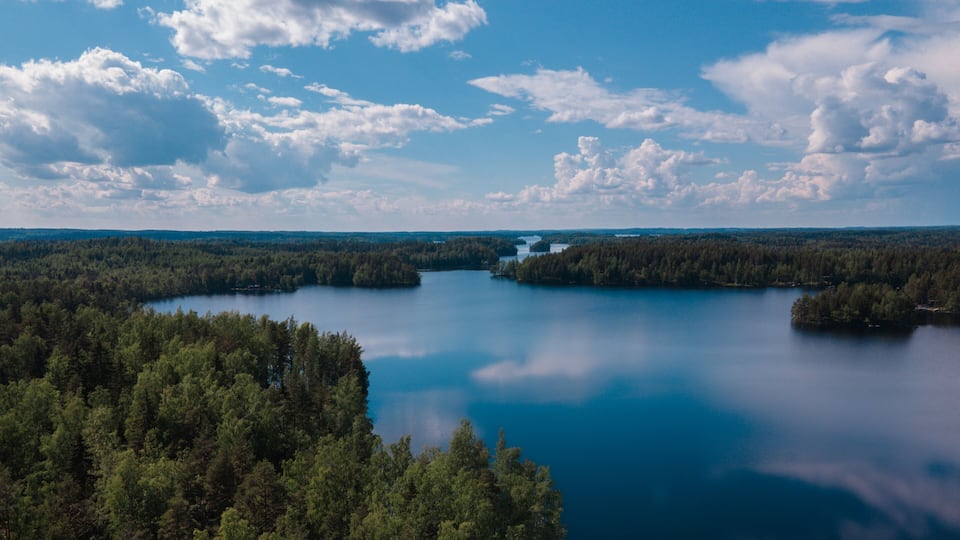 A lake surrounded by dense forests and a clear sky with scattered clouds.