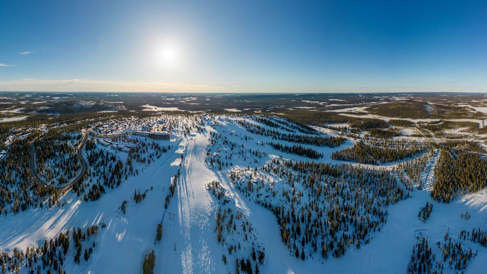 A snow-covered mountainous landscape with ski trails and a clear sky.