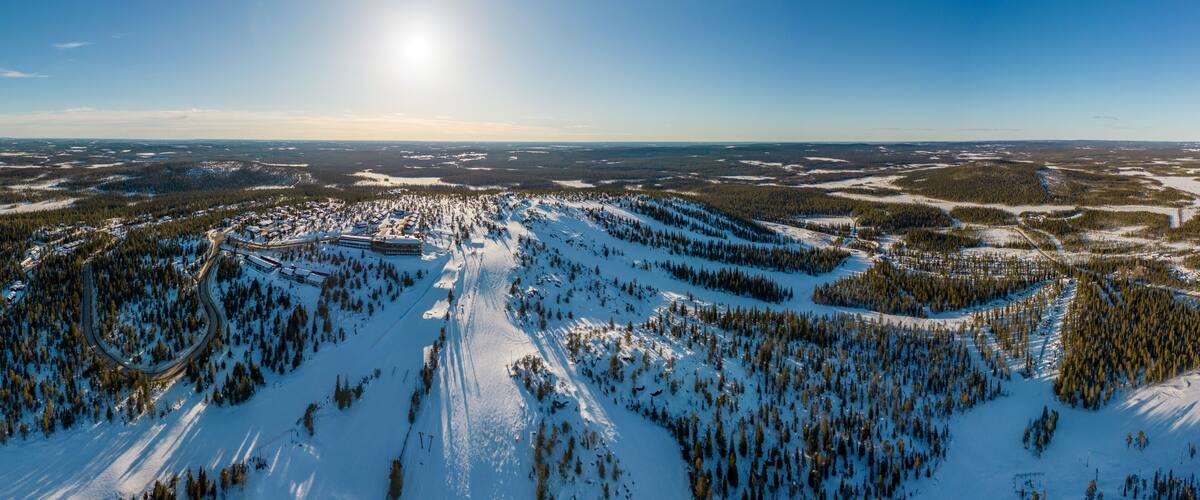 A snow-covered mountainous landscape with ski trails and a clear sky.