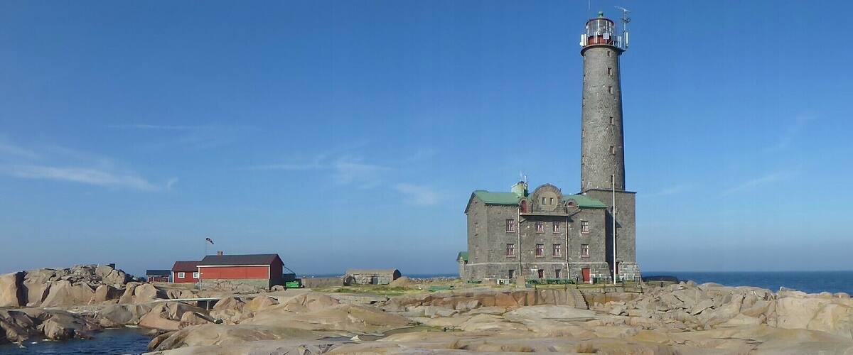A lighthouse on a rocky shore with a red building nearby.