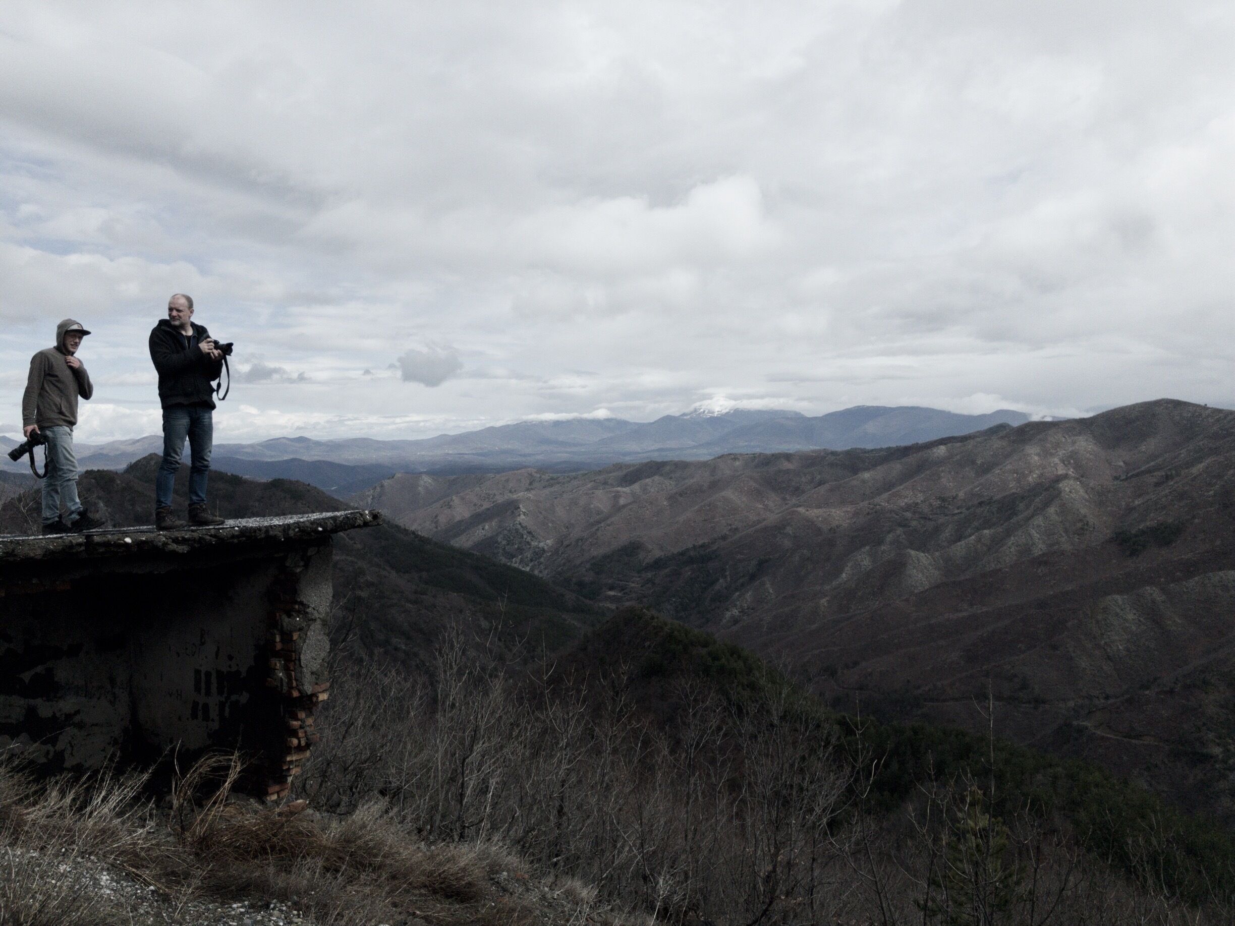 Two people standing on a cliff overlooking a mountainous landscape.